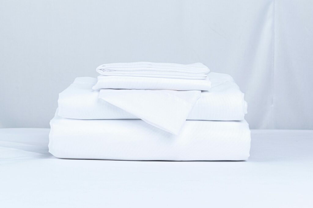 pexels-photo-31902663-31902663 A neatly folded stack of crisp white bed linens on a clean surface.